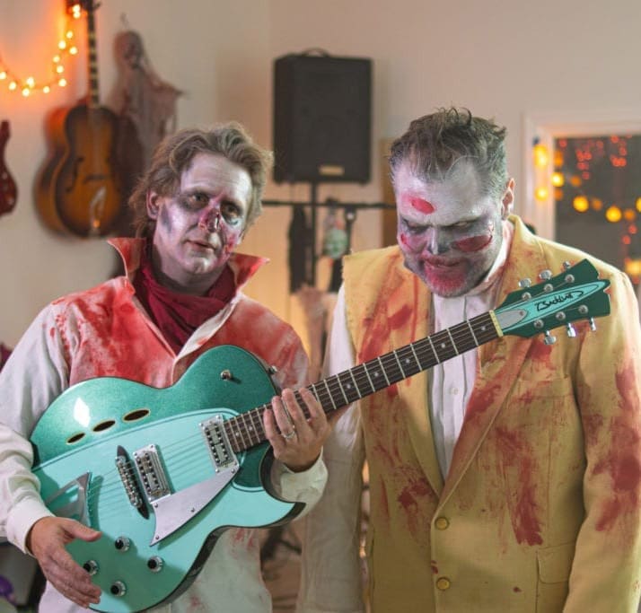 Two men dressed as zombies holding an electric guitar