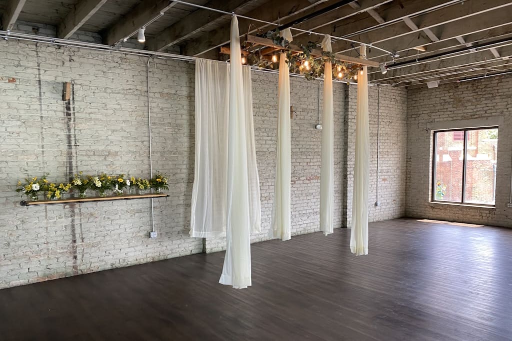 Sparse room with old white brick, hardwood floors, hanging curtains, and flowers