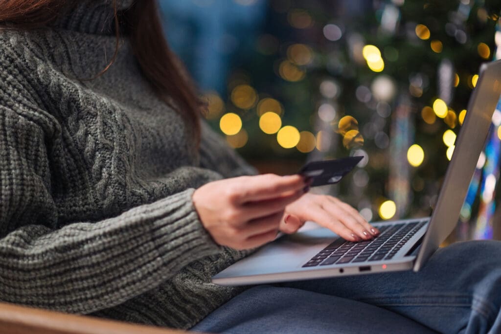 How to boost ecommerce sales during the holidays. Online shopping, sales and discounts promotions during winter holidays, online shopping at home. Female hands on the laptop with credit card and blurred bokeh lights